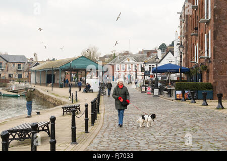 Exeter Quayside - una donna di mezza età a piedi il suo cane lungo il lato del fiume Exe in inverno Foto Stock