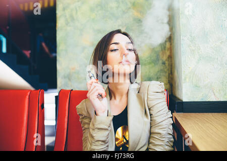 La ragazza si siede e fuma sigaretta elettronica Foto Stock