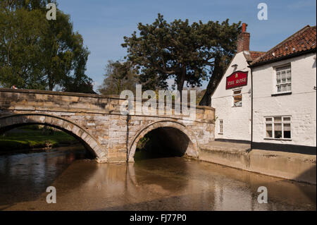Un waterside pub, il Rose Inn, (Pickering, North Yorkshire, Inghilterra, Regno Unito) sorge accanto a un vecchio, pietra ponte arcuato spanning Pickering Beck. Foto Stock
