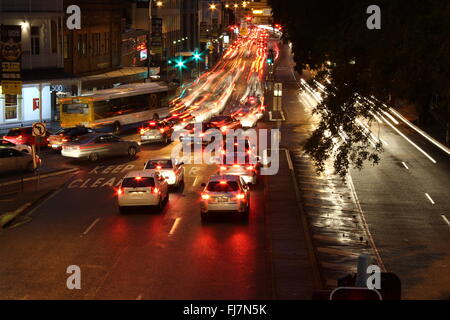 Di sera la città interna traffico dell'ora di punta in condizioni di bagnato in elevazione con percorsi di luce del traffico sul lato sinistro della strada Foto Stock