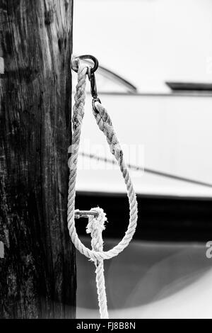 Frammento di cima nautica recinto con legno stagionato post nel porto di Key West, Florida, barche ancorate in background.un nero Foto Stock