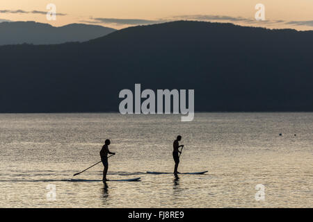 Silhouette di 2 stand up paddle boarders al tramonto lungo le coste di un paradiso tropicale isola in acque calme. Foto Stock