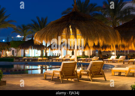 SHARM EL SHEIKH, Egitto - 27 febbraio 2014: Febbraio notte sulla spiaggia, ombrelloni di paglia e lettini in piscina presso l'hotel essere Foto Stock