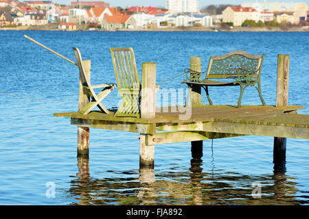 Una serie di vecchi mobili da esterno stand sull'estremità di un molo in legno con il paesaggio al di fuori della messa a fuoco in background. Foto Stock