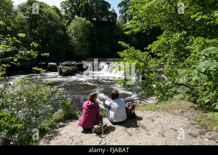 Due donne relax sotto il sole a Aysgarth Falls, Yorkshire Dales, nello Yorkshire, Inghilterra, Regno Unito, Europa Foto Stock