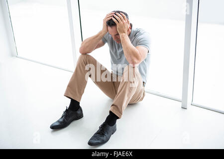 Tensionata uomo seduto contro la finestra Foto Stock