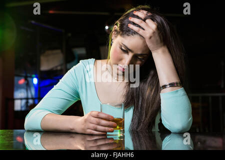 Premuto donna avente whiskey al bancone bar Foto Stock