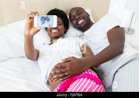 Coppia felice di toccare la pancia incinta prendendo selfie Foto Stock