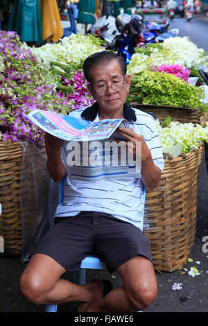 L'uomo la lettura della carta in una Bangkok il mercato dei fiori Foto Stock