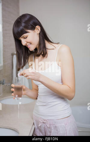 Bella donna messa pillola in un bicchiere di acqua Foto Stock