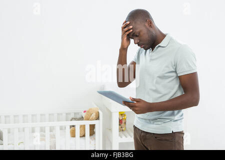 Tensionata uomo in piedi accanto a una culla e utilizzo di tavoletta digitale Foto Stock