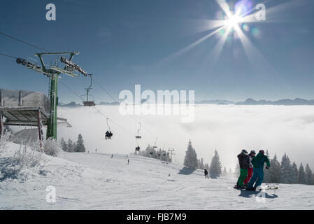 Gli sciatori in piedi accanto ad una sedia di sollevamento anteriore del panorama alpino a Brauneck ski resort in condizioni di luce solare intensa,Baviera,Germania Foto Stock