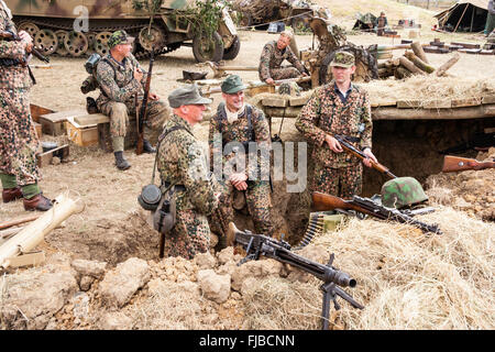 Guerra e Pace Show, Inghilterra. La seconda guerra mondiale la rievocazione. Il tedesco battle group indossando il camuffamento dot tuniche, relax intorno posizione consolidate Foto Stock