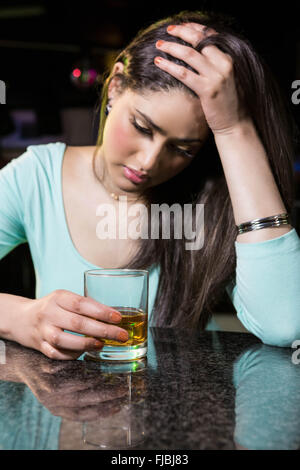 Premuto donna avente whiskey al bancone bar Foto Stock