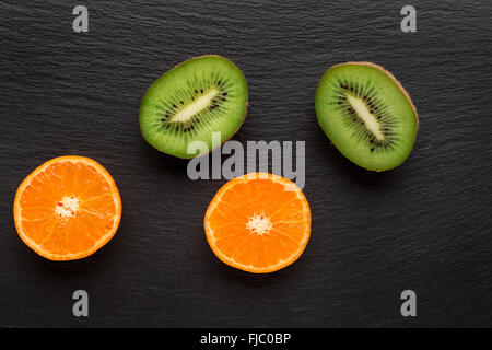 Kiwi e mandarino su pietra scura sullo sfondo. Vista superiore Foto Stock