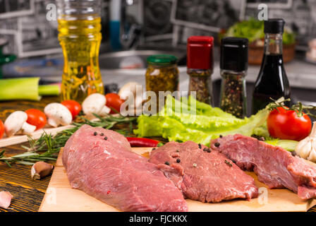 Tre pezzi di carne cruda sul tavolo di essere stagionato e preparati per la cucina con le erbe e olio in background Foto Stock