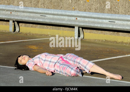 Luglio 2015 - giovane donna playing dead in pigiama sulla parte superiore di un parcheggio multipiano dell'hotel Foto Stock