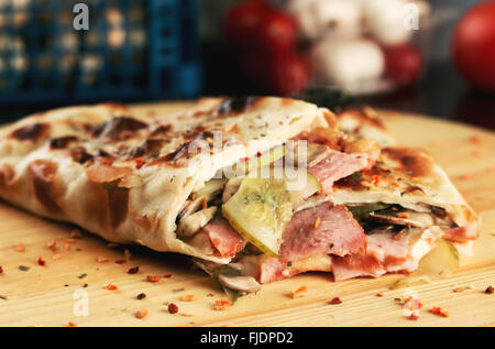 Una gustosa pizza rotoli chiuso pizza calzone con prosciutto, funghi e il cetriolo. Profondità di campo Foto Stock