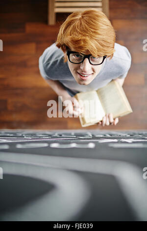 Scolaro con un libro in mano in piedi vicino alla lavagna Foto Stock