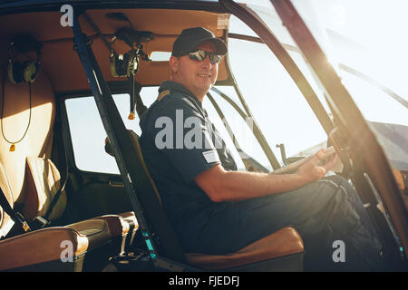 Ritratto di felice pilota maschile seduto in cabina di pilotaggio di un elicottero con una mappa per aviazione. Foto Stock