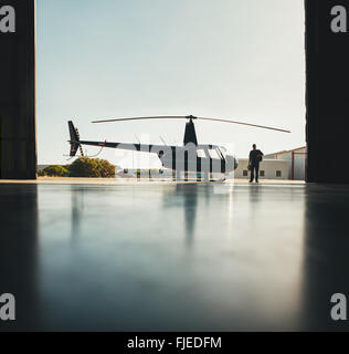 Silhouette di un elicottero con un pilota a piedi in hangar aereo dopo il volo. Foto Stock