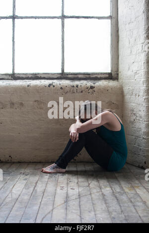 Triste donna giovane seduto sul pavimento in legno mediante la finestra Foto Stock