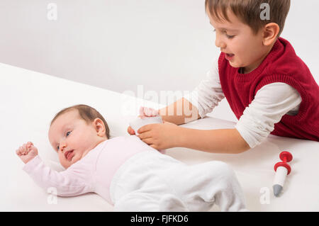 Fratello di pagare come medico e paziente con il suo bambino sorella. Il ragazzo si lega la sua mano con bendaggio. Foto Stock