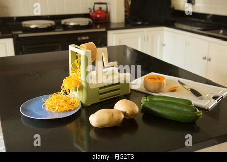 Rendendo la zucchina tagliatelle o 'courgetti' in una cucina della famiglia usando un spiralizer con altri ortaggi e legumi Foto Stock