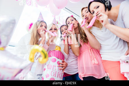 Il gruppo di donne sul baby shower party divertirsi indossando cappelli di partito di soffiaggio streamer di carta Foto Stock