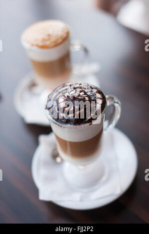 Due tazze di latte o caffè sono in piedi su una tabella di colore marrone nella caffetteria. Foto Stock