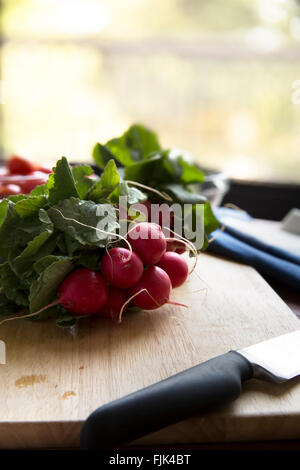 Mazzetto di intere ravanelli sul tagliere con un coltello, orientamento verticale Foto Stock