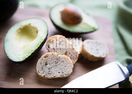 Avocado fresco tagliato a metà e piccole fette di pane per la realizzazione di avocado toast. Foto Stock