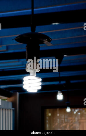 Accesa con luce a risparmio energetico la lampadina che pendono dal soffitto blu con sfocatura sbiadito e lampadine e riflessioni ulteriori. Foto Stock