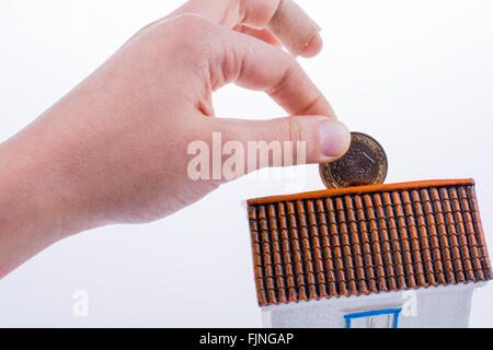 Mano moneta caduta nel salvadanaio a forma di un modello di casa Foto Stock