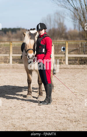 Ragazza in piedi accanto a un fiordo cavallo nel maneggio e tenendo il pony la briglia Foto Stock