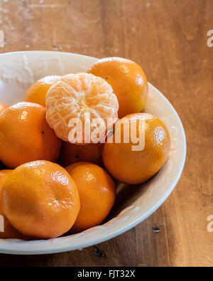 Mandarini arance, Citrus reticulata, con uno pelato in una ciotola bianco. Foto Stock