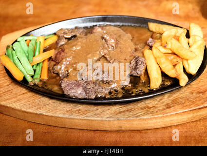 Grigliata di buffalo bistecca con verdure e patate in padella sul tavolo di legno Foto Stock