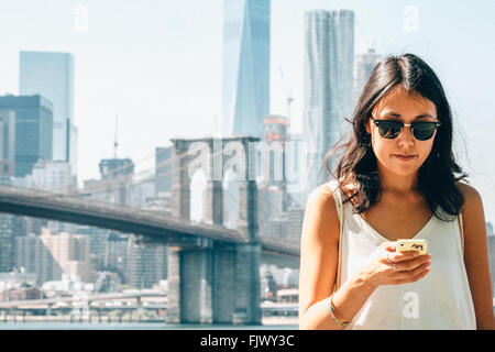Giovane donna utilizzando Smart Phone contro il ponte di Brooklyn
