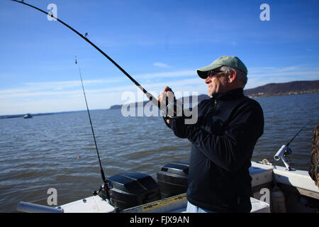 L'uomo la bobinatura nel pesce della parte posteriore di una barca sul fiume Hudson, New York Foto Stock