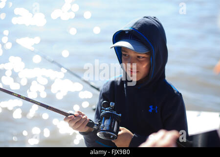 Ragazzo giovane azienda asta di pesca su una barca Foto Stock