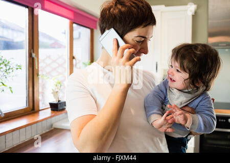 Carino madre sul telefono e tenere il bambino Foto Stock