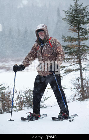 Senior uomo nel camuffamento di rivestire le racchette da neve in un giorno di neve nei boschi del nord del Maine vicino Rangeley. Foto Stock