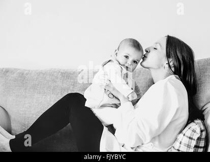Giovane mamma baciando la sua bambina sul divano di casa Foto Stock