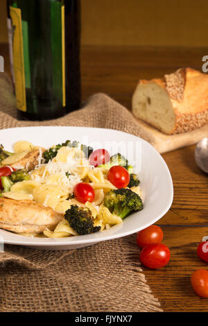 Pasto italiano autentico con fatti in casa orecchiette, pollo, broccoli, i pomodori. Filone di pane italiano e una bottiglia di vino in Foto Stock