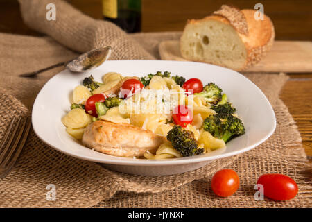 Pasto italiano autentico con fatti in casa orecchiette, pollo, broccoli, i pomodori. Filone di pane italiano e una bottiglia di vino in Foto Stock