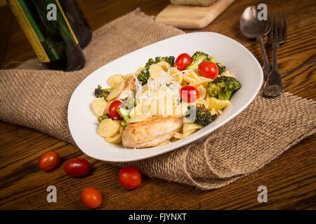 Pasto italiano autentico con fatti in casa orecchiette, pollo, broccoli, i pomodori. Filone di pane italiano e una bottiglia di vino in Foto Stock