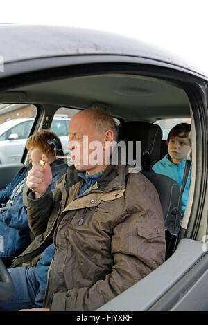 Uomo di fumare con bambini in suo automobile Foto Stock