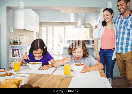 Bambini aventi la prima colazione mentre i genitori in piedi dalla tabella Foto Stock
