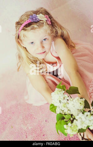 Bellissima ragazza con lunghi capelli biondi holding fiori indossando home fatto a mano con archetto Foto Stock