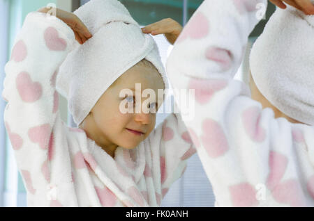 Bella ragazza in accappatoio con asciugamano nei suoi capelli sorridendo a se stessa nello specchio Foto Stock